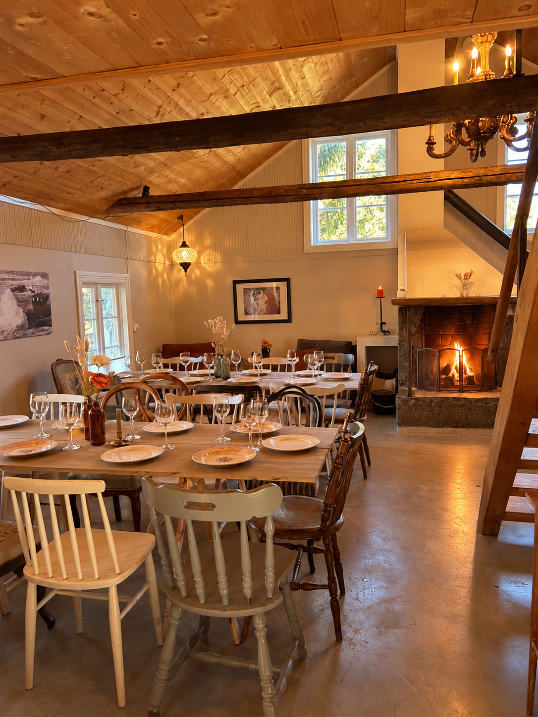 Fjøset with a set long table, timber beams and a fire in the fireplace